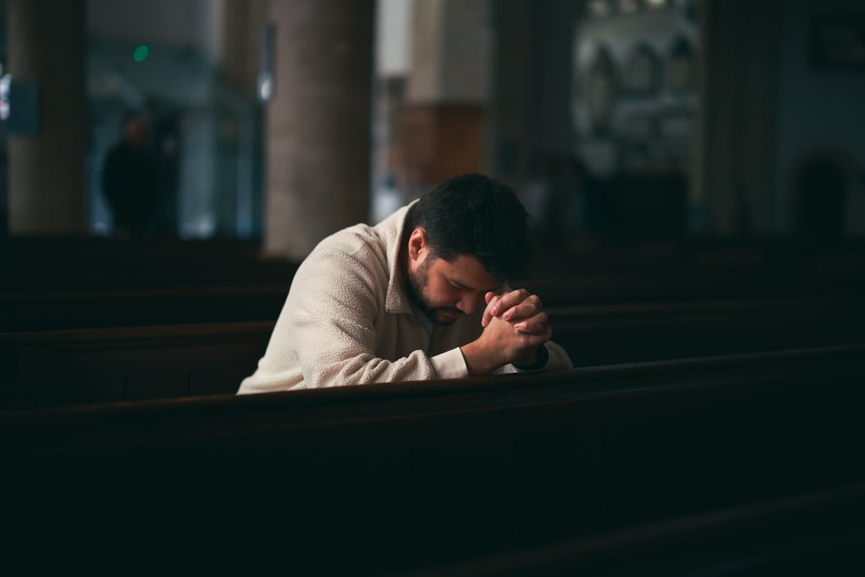 young man sitting on the pews of the dark church, profile portrait in a religious interior