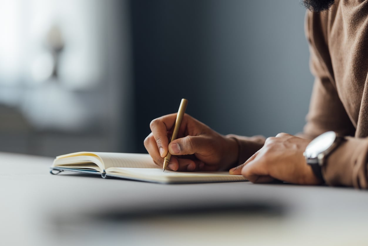 close up of man writing in a notebook at a desk